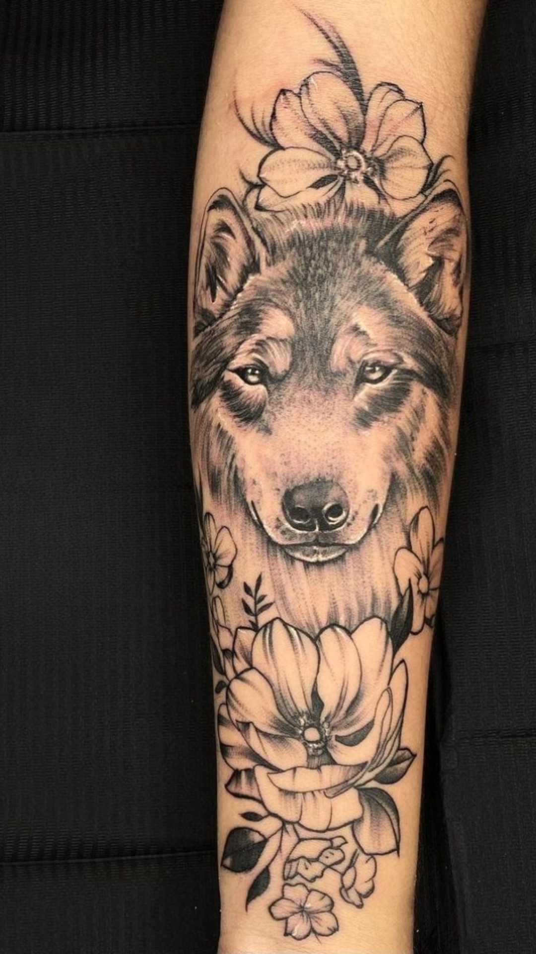 Black and grey wolf portrait with fine-line flowers on forearm
