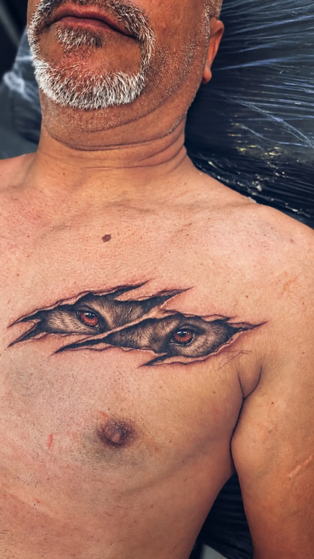 Realism tattoo of eyes peering through torn skin on chest