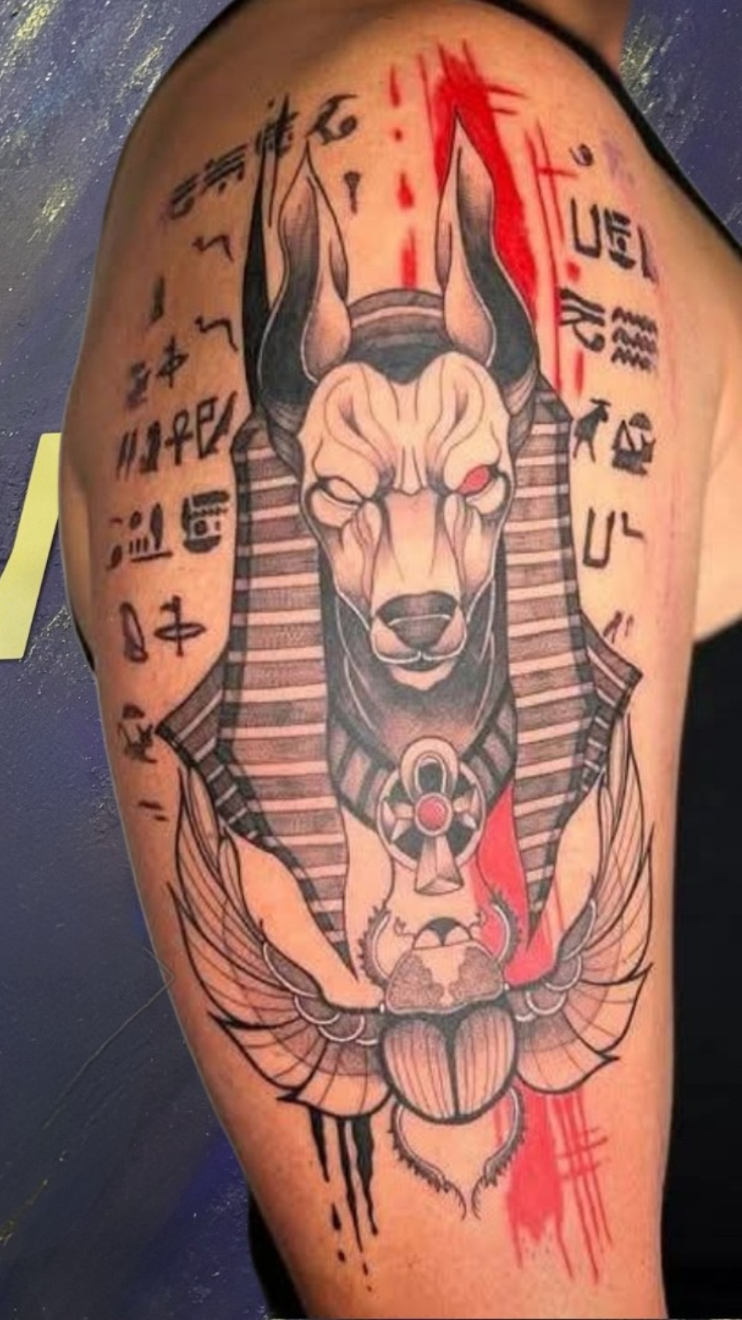 Anubis tattoo with red ink splashes on upper arm